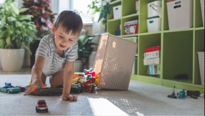 A cheerful European boy plays with colorful cars on the carpet in his room. 