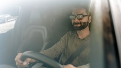 Confident businessman driving a car on a sunny day. Looking relaxed and happy. Wearing sunglasses.