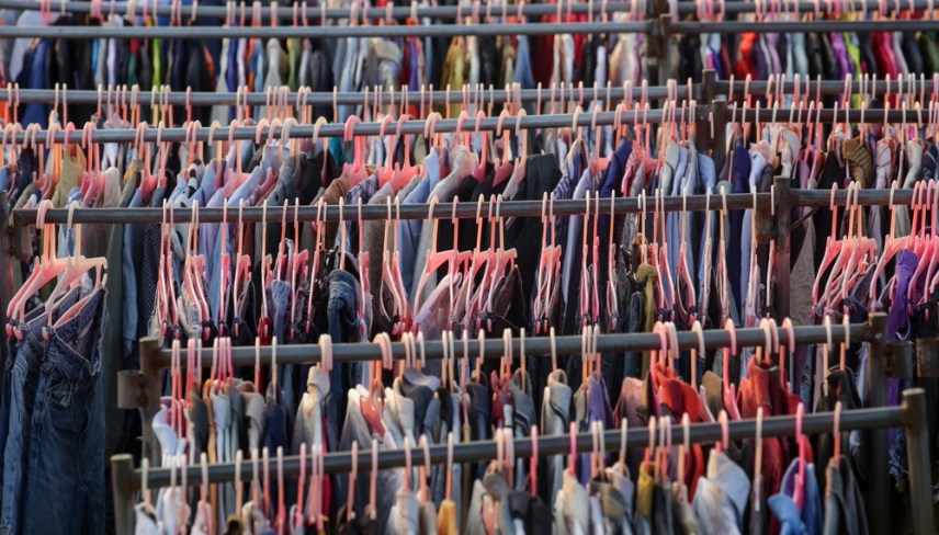 Huge selection of different used clothes for men, women and children on the rack in a second hand shop or thrift store. Concept of waste problem in fashion industry.