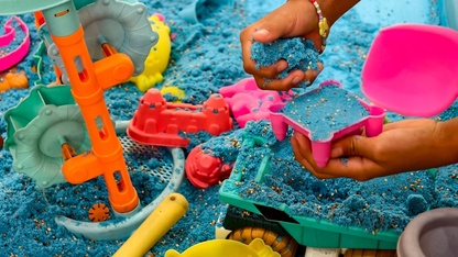 A child's hand plays with blue kinetic sand.