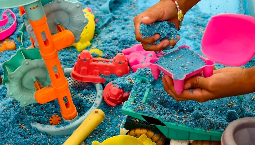 A child's hand plays with blue kinetic sand.