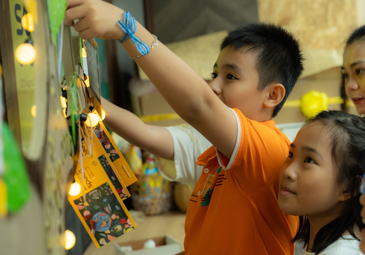 Two children hang a craft piece on a decorated wall. 