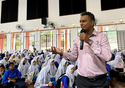 An Intertek colleague holding a microphone addresses a hall full of school students. 