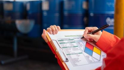 Chemical worker completing a Chemical Hazardous Materials identification form on a clipboard in an industrial facility.